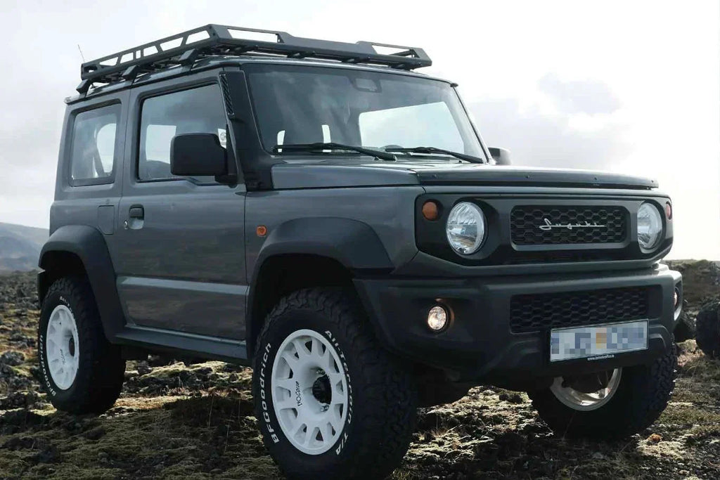 Suzuki Jimny (2018+) with 16" EVO Corse DakarZero wheels in white mounted on BF Goodrich KO2 tyres and various accessories such as retro grille and vintage emblem.